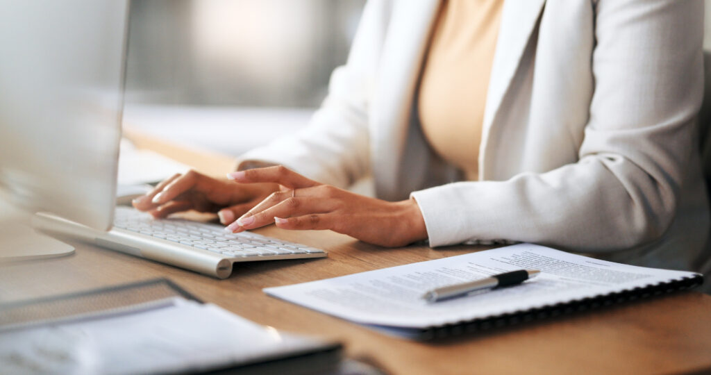 closeup of the hands of a receptionist typing and sending emails while working in an office alone. one secretary doing admin and writing reports while organizing a schedule for her manager at work